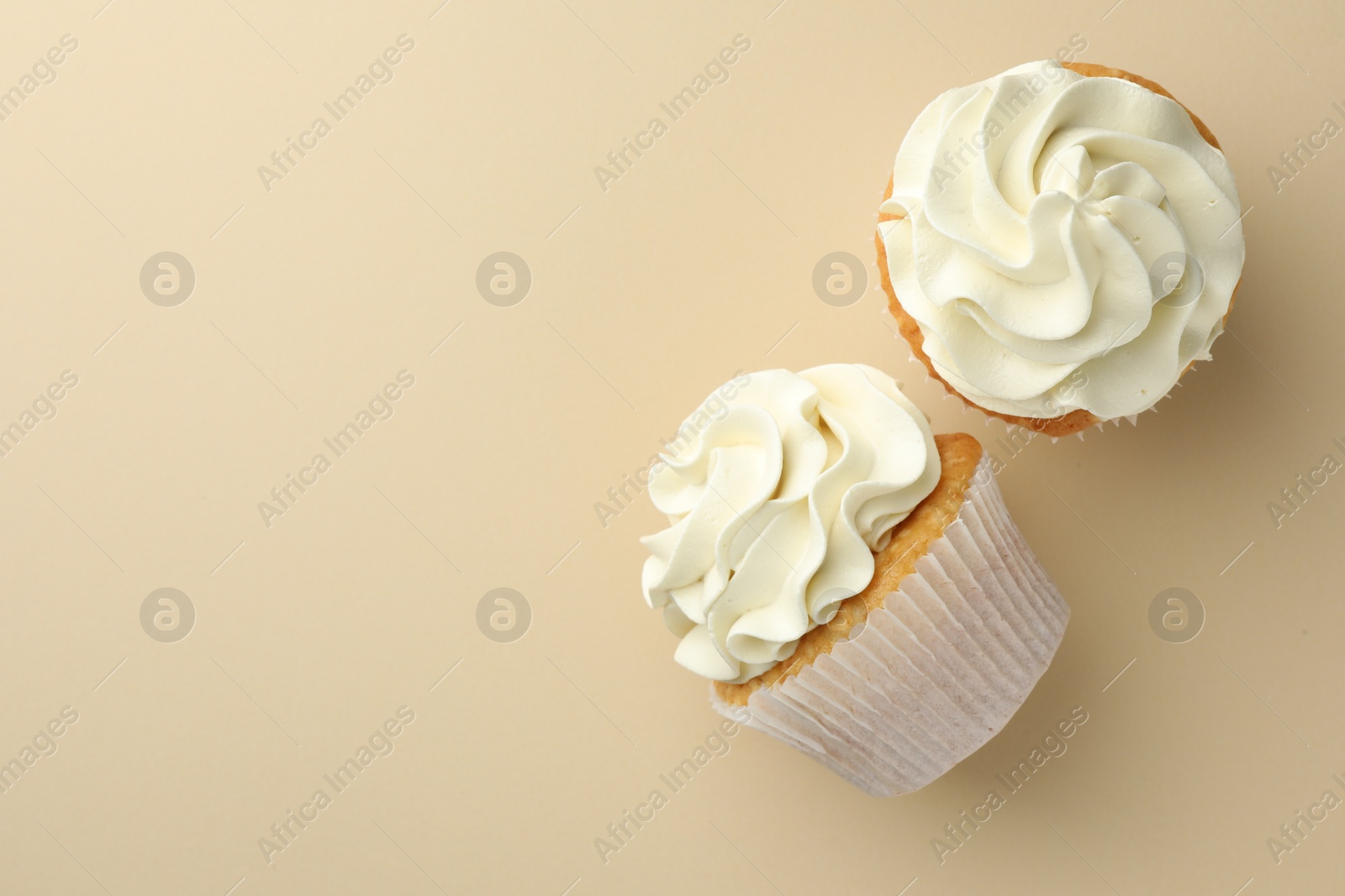 Photo of Tasty vanilla cupcakes with cream on beige background, top view. Space for text