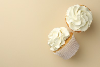 Tasty vanilla cupcakes with cream on beige background, top view. Space for text