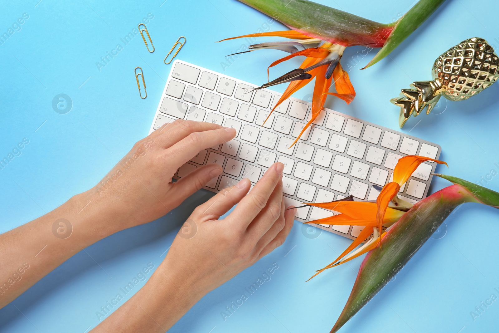 Photo of Woman using computer keyboard on table decorated with tropical flowers, top view. Creative design ideas