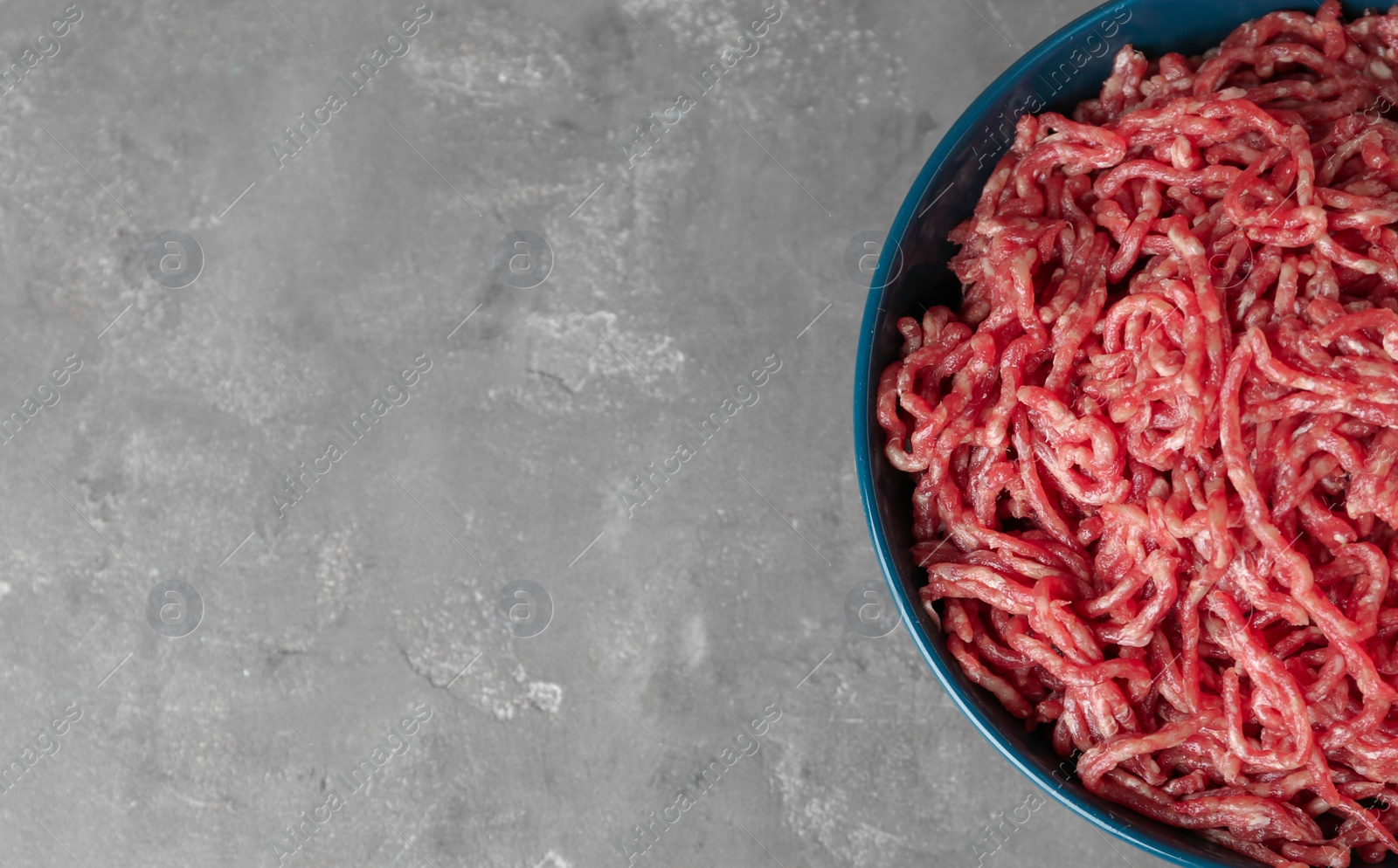 Photo of Bowl of raw minced meat on grey table, top view. Space for text