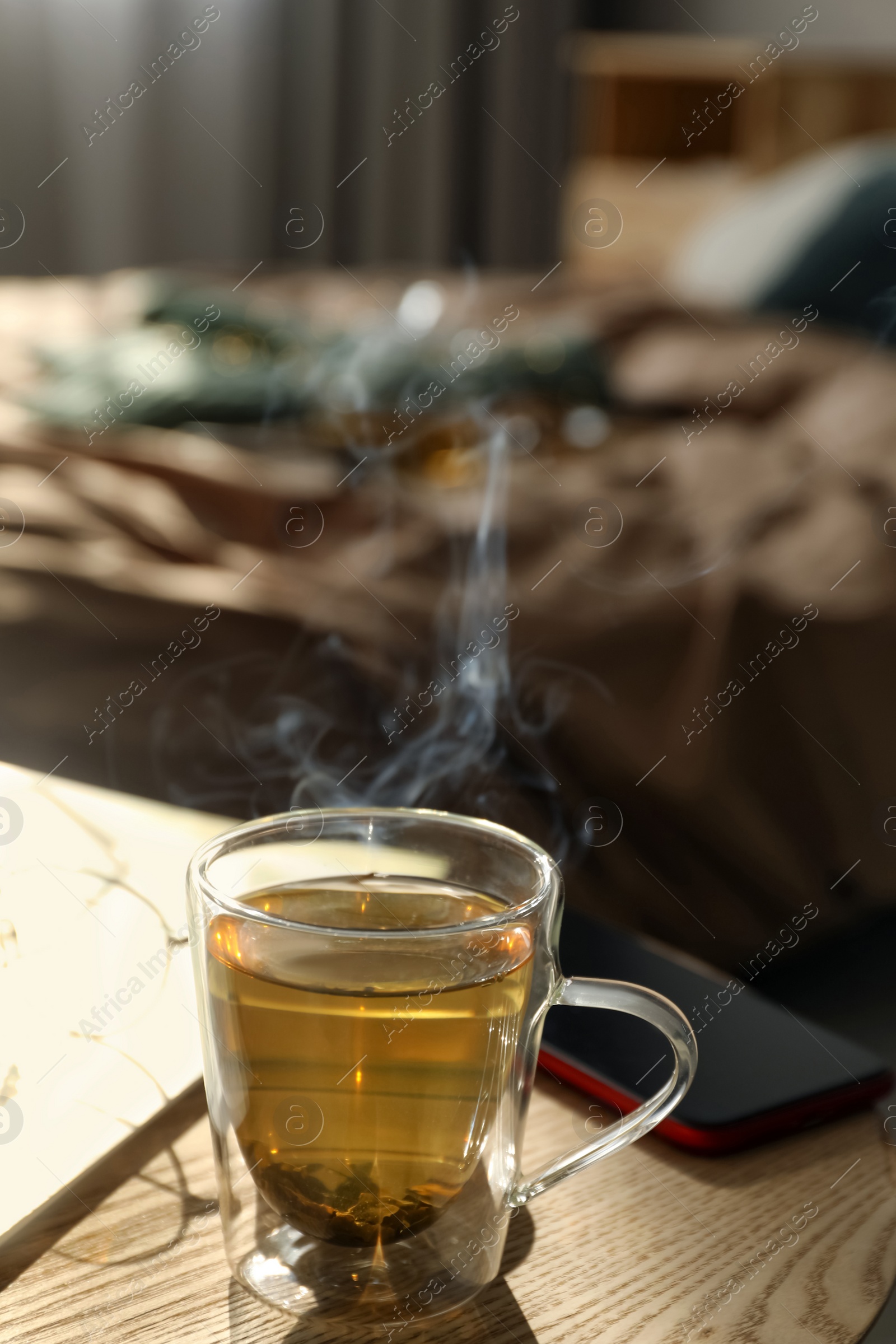 Photo of Glass cup of freshly brewed tea on wooden table in bedroom. Cozy home atmosphere