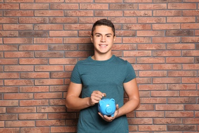 Teenage boy putting coin into piggy bank near brick wall