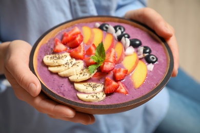 Woman holding bowl with tasty acai smoothie and fruits on blurred background, closeup