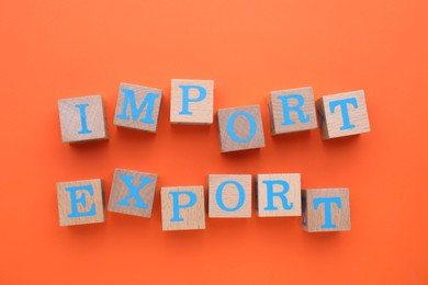Words Import and Export made of wooden cubes on orange background, top view