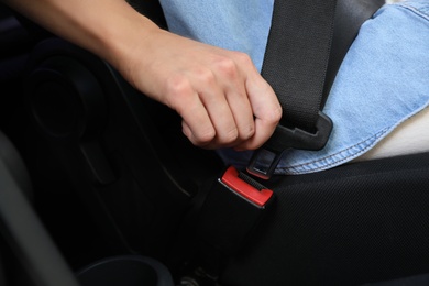 Woman fastening safety belt on driver's seat in car, closeup