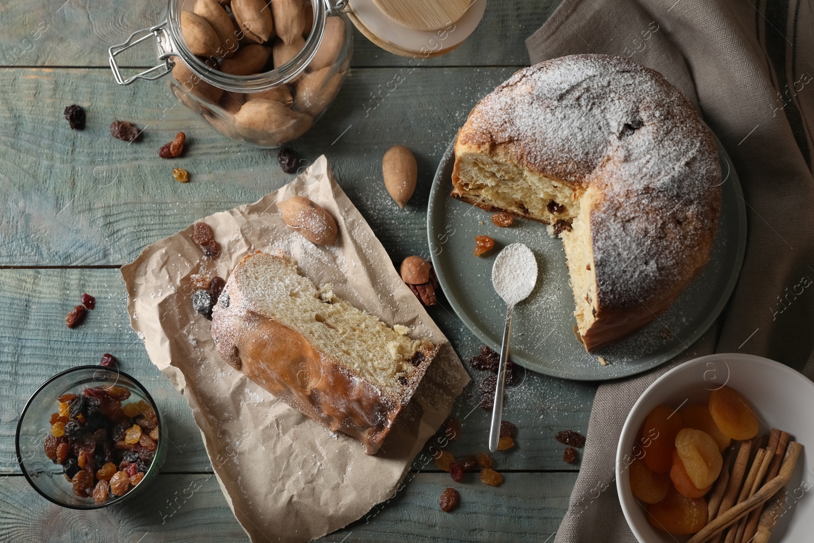 Photo of Delicious cut Panettone cake with powdered sugar and raisins on light blue wooden table, flat lay. Traditional Italian pastry