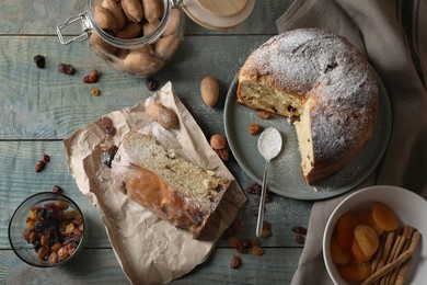 Photo of Delicious cut Panettone cake with powdered sugar and raisins on light blue wooden table, flat lay. Traditional Italian pastry
