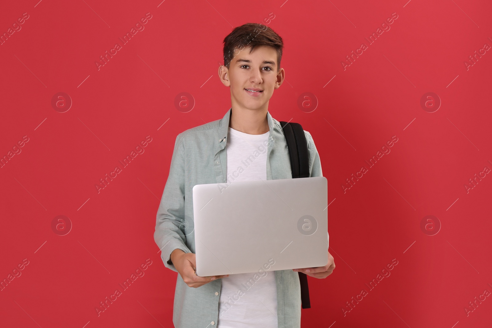 Photo of Teenage student with backpack and laptop on red background