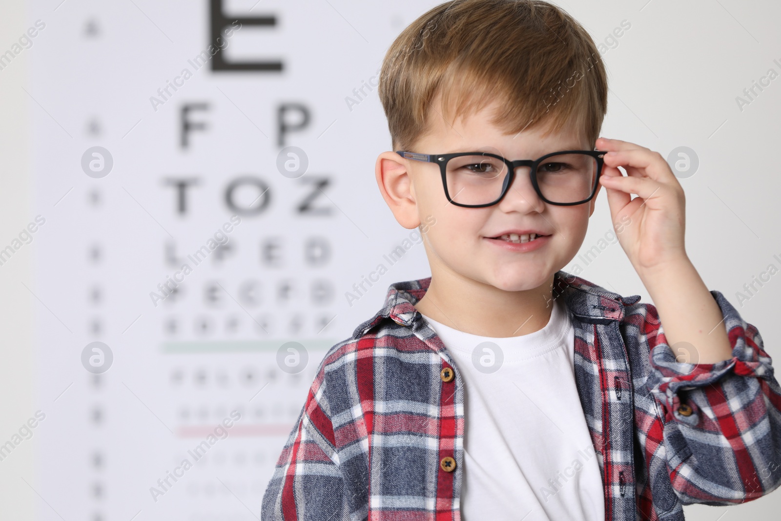 Photo of Little boy with glasses against vision test chart