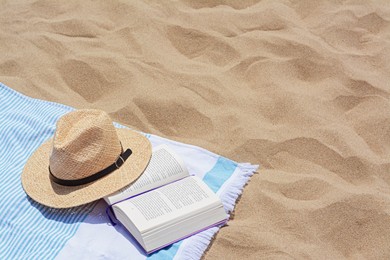 Photo of Beach towel with open book and straw hat on sand, space for text