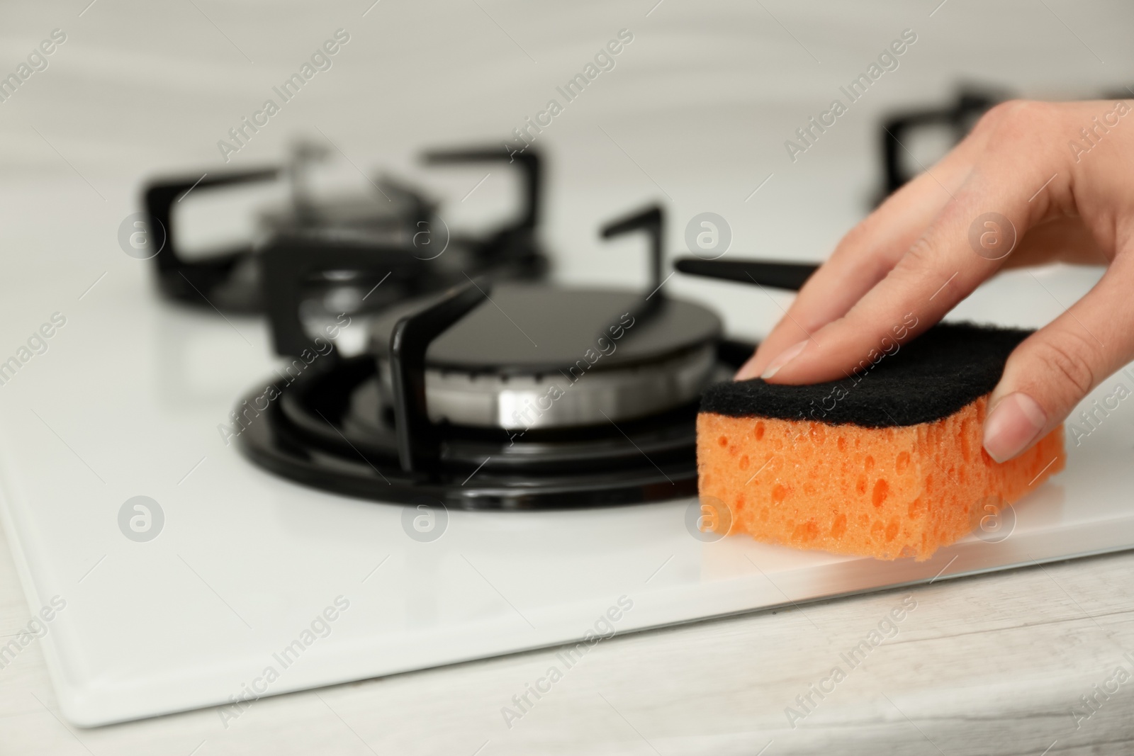 Photo of Woman cleaning gas stove with sponge, closeup