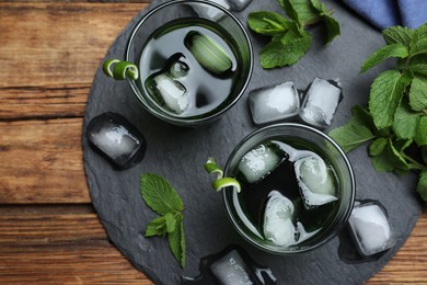 Photo of Delicious mint liquor with ice cubes and green leaves on wooden table, flat lay