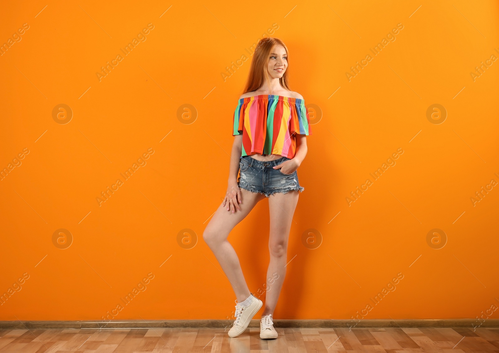 Photo of Young woman in stylish jean shorts near color wall