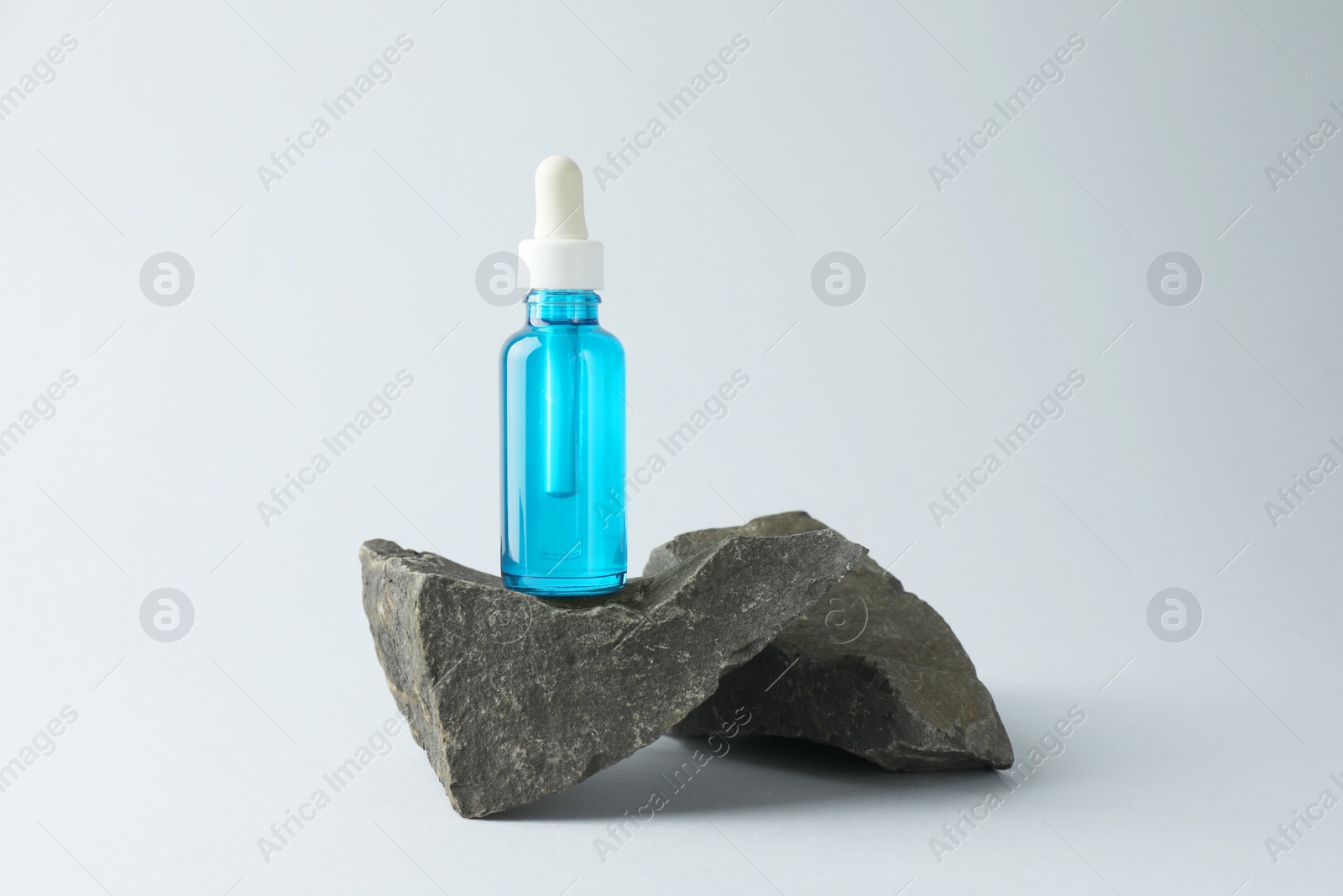 Photo of Bottle of cosmetic serum on stone against light grey background