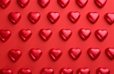 Photo of Heart shaped chocolate candies on red background, flat lay