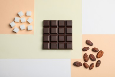 Delicious dark chocolate bar, refined sugar and cocoa beans on color background, flat lay