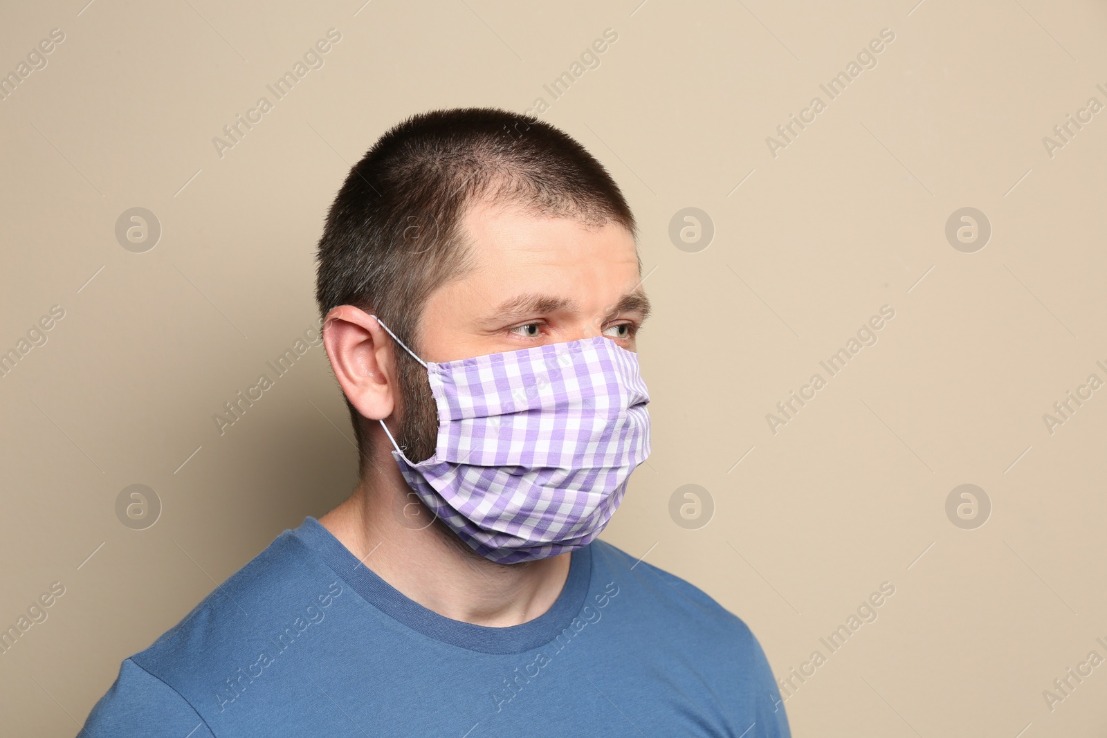 Photo of Man wearing handmade cloth mask on beige background. Personal protective equipment during COVID-19 pandemic