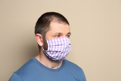 Man wearing handmade cloth mask on beige background. Personal protective equipment during COVID-19 pandemic