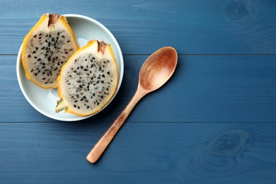 Photo of Plate with delicious cut dragon fruit (pitahaya) and spoon on blue wooden table, flat lay. Space for text