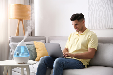 Photo of Man using laptop in room with modern air humidifier