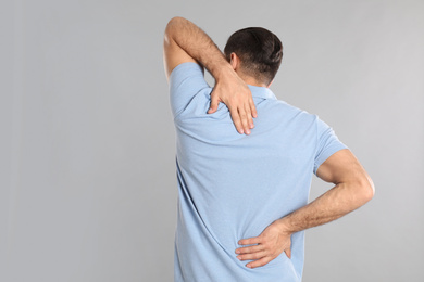 Photo of Man suffering from pain in back on light grey background. Visiting orthopedist