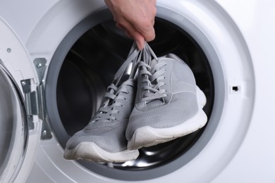 Photo of Woman putting pair of sport shoes into washing machine, closeup