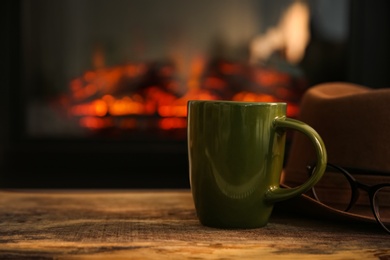 Photo of Green cup with hot drink on wooden table against fireplace, space for text