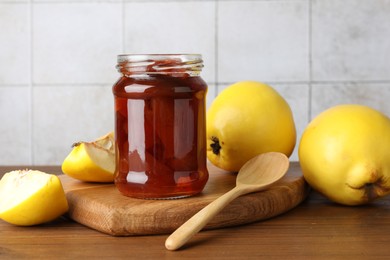 Photo of Tasty homemade quince jam in jar, spoon and fruits on wooden table