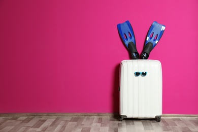 Suitcase with swim fins on floor near color wall. Space for design