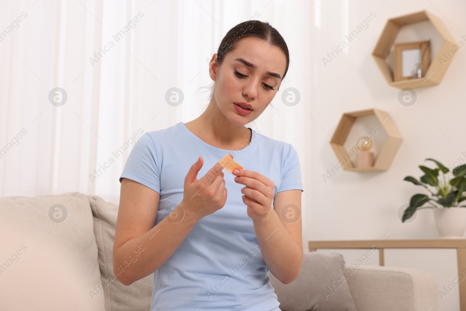 Photo of Woman putting sticking plaster onto finger at home