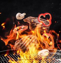 Image of Meat, mushrooms and bell pepper slices falling onto barbecue grill with flame against black background, closeup