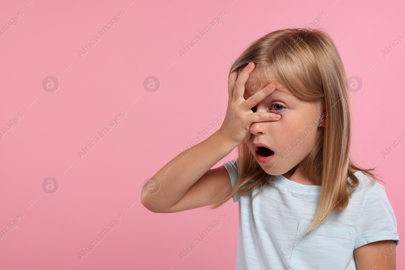 Photo of Embarrassed little girl covering face with hand on pink background. Space for text