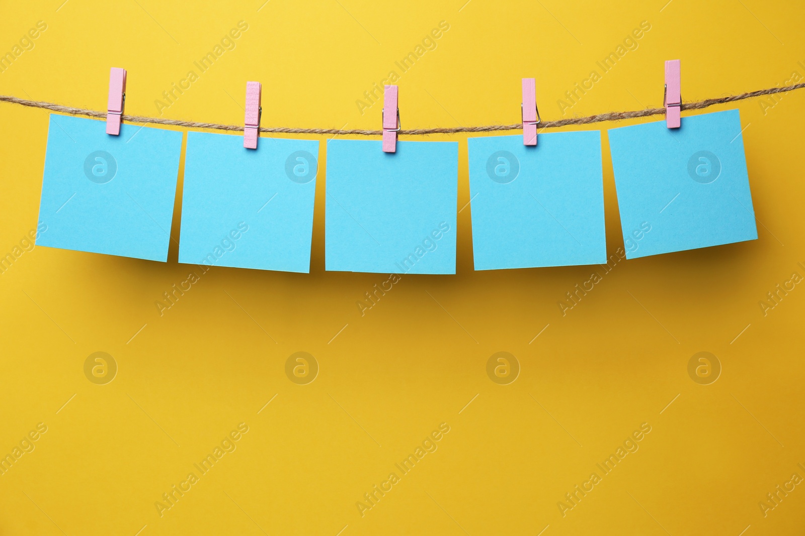 Photo of Wooden clothespins with blank notepapers on twine against yellow background. Space for text