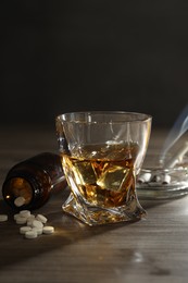 Photo of Alcohol addiction. Whiskey in glass, pills and cigarettes on wooden table