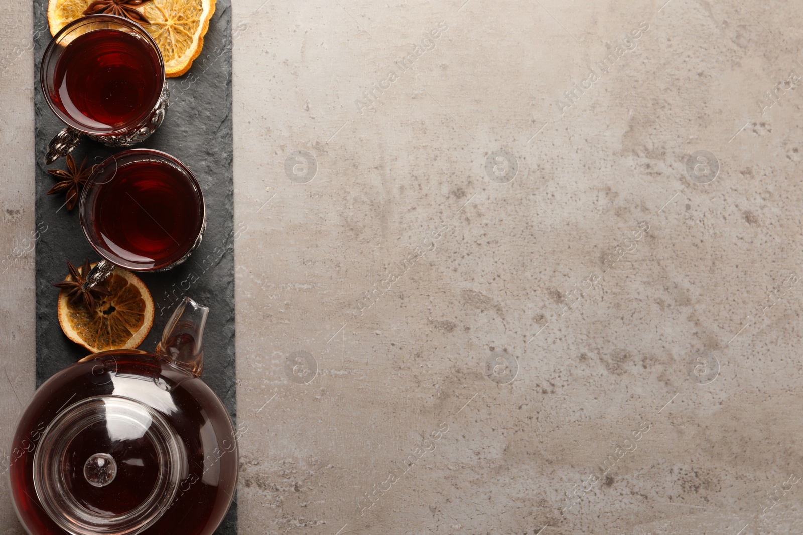 Photo of Slate plate with glasses of traditional Turkish tea in vintage holders, pot, dried orange and anise on light grey table, top view. Space for text