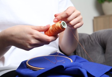 Photo of Woman with spool of thread embroidering on cloth at home, closeup