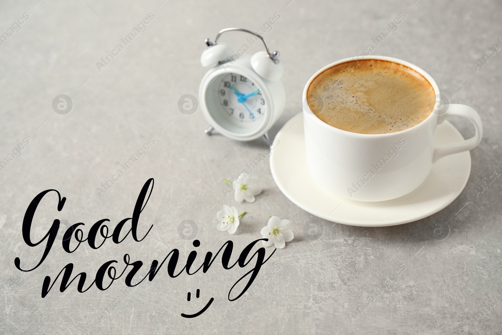 Image of Cup of coffee, flowers and alarm clock on light grey table. Good morning