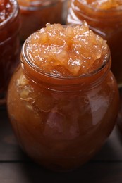 Photo of Delicious apple jam in jars on wooden table, closeup