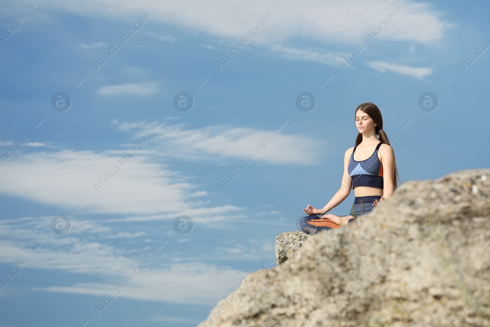 Photo of Teenage girl meditating on cliff against blue sky. Space for text