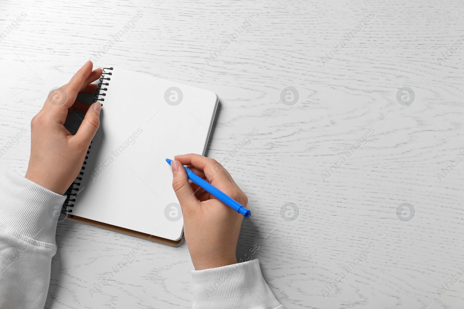 Photo of Woman writing in notebook with pen at white wooden table, top view. Space for text