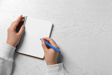 Photo of Woman writing in notebook with pen at white wooden table, top view. Space for text