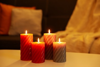 Photo of Beautiful candles on white table near sofa indoors. Cosy atmosphere