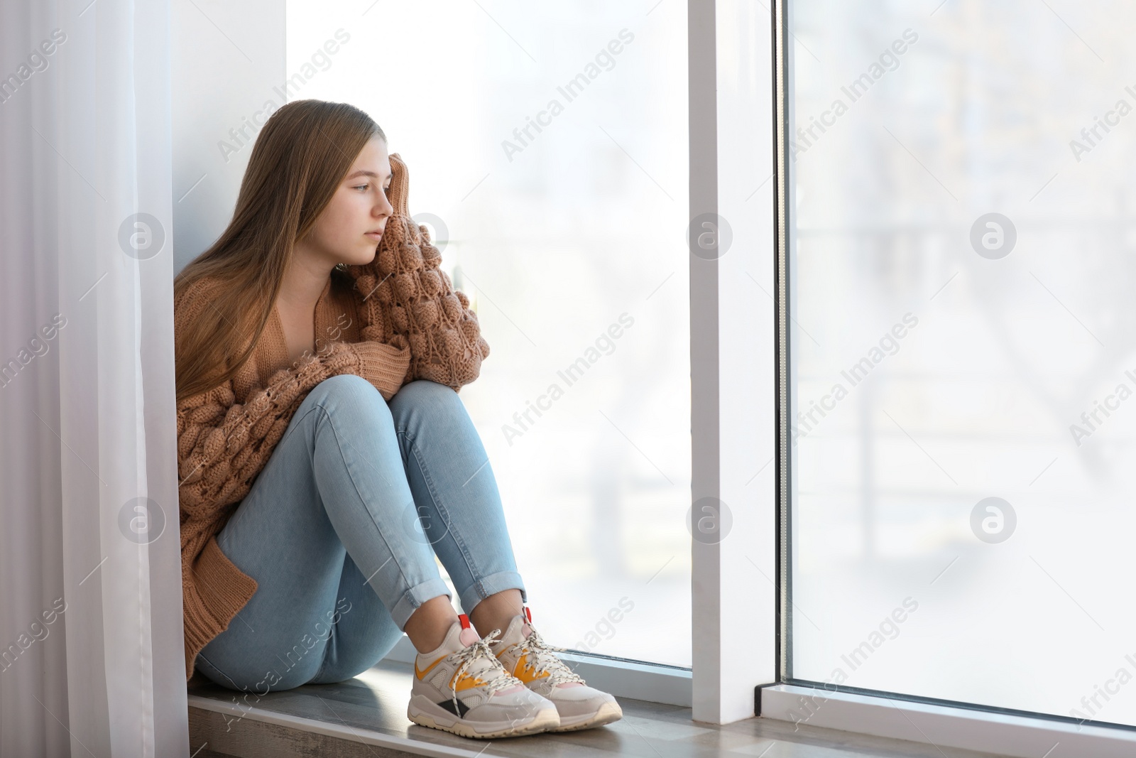 Photo of Upset teenage girl sitting alone near window indoors