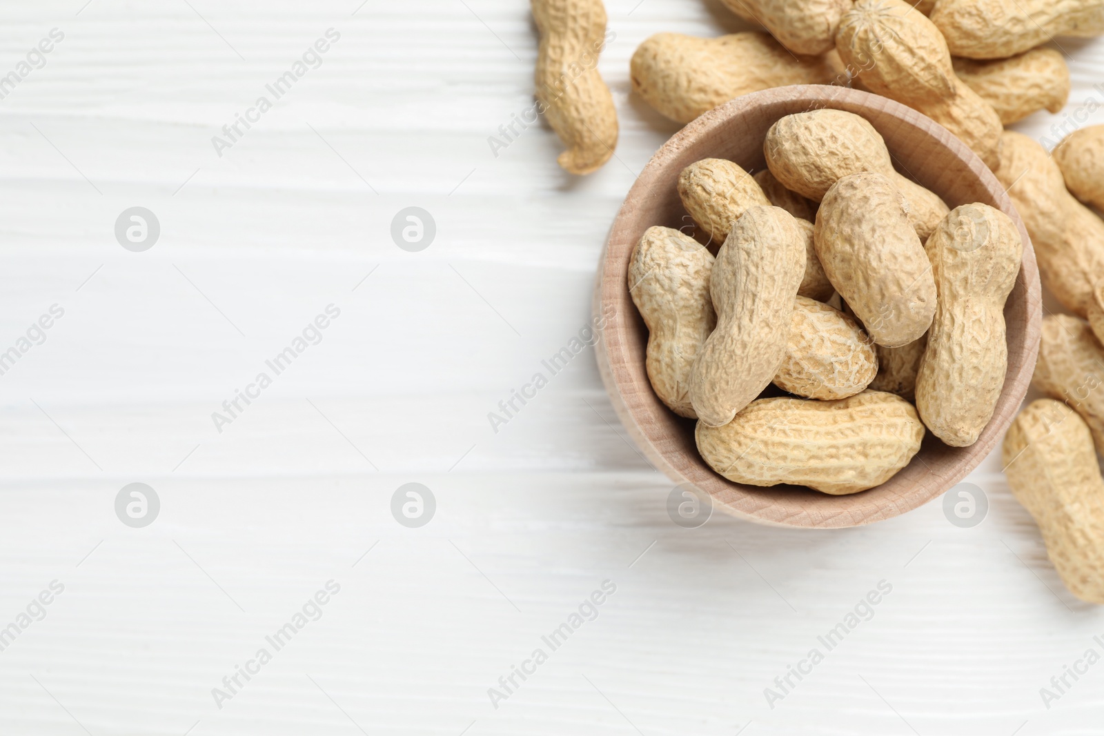 Photo of Fresh peanuts in bowl on white wooden table, top view. Space for text