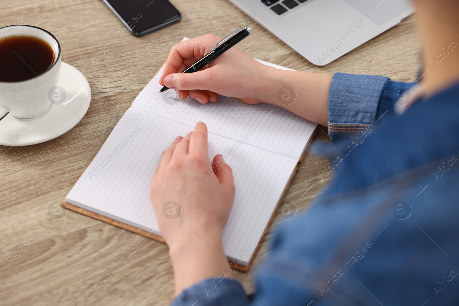 Photo of Young woman writing in notebook at wooden table, closeup