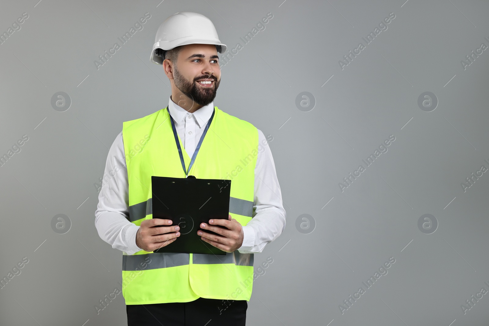 Photo of Engineer in hard hat holding clipboard on grey background, space for text