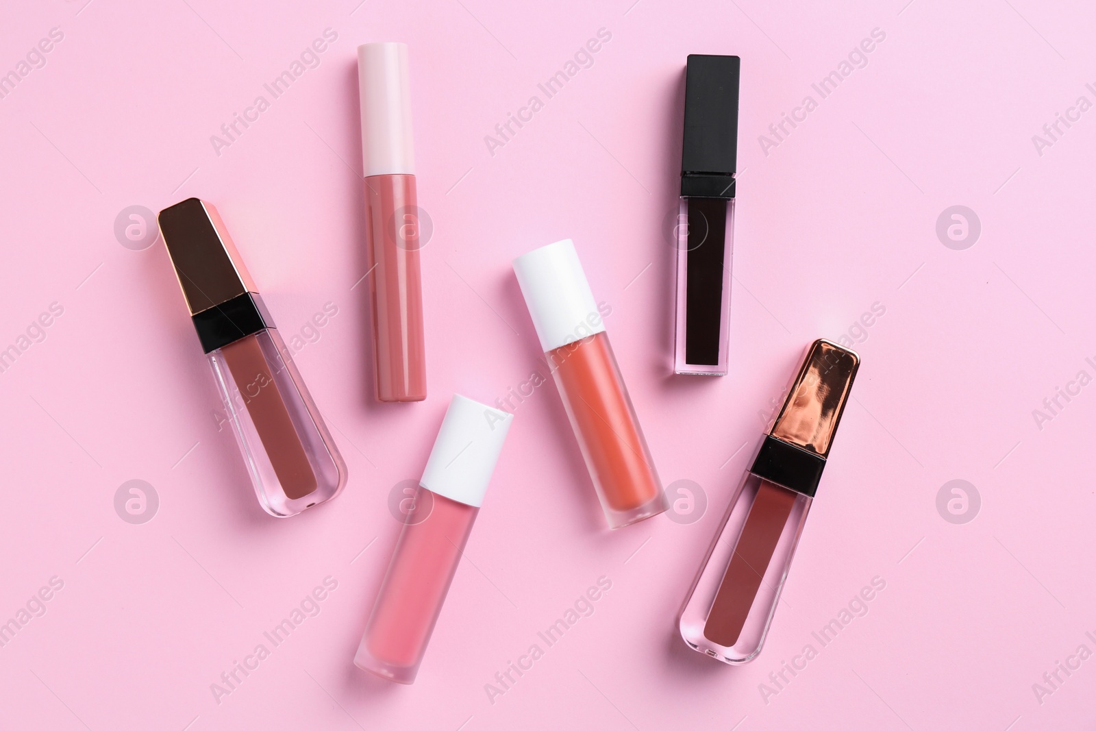 Photo of Different lip glosses on pink background, flat lay