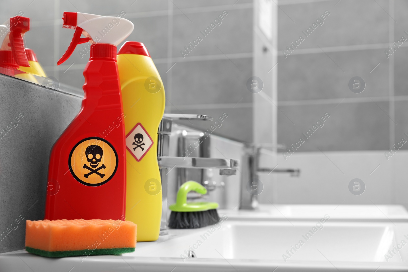 Photo of Bottles of toxic household chemicals with warning signs, brush and scouring sponge in bathroom, space for text