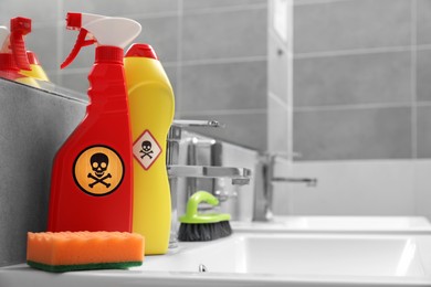 Photo of Bottles of toxic household chemicals with warning signs, brush and scouring sponge in bathroom, space for text