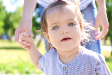 Photo of Adorable baby girl holding mother's hand while learning to walk outdoors
